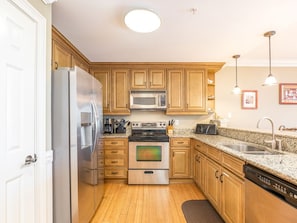 Efficient kitchen with refrigerator, microwave, oven, and dishwasher, featuring a granite countertop and pendant lights.
