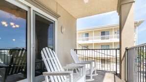 A balcony with two rocking chairs, a glass door, and a view of a building across the street. - Silver Seas 203 by Tybee Vacation Rentals (Tybee Island)