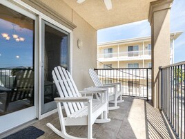 Un balcon avec deux fauteuils à bascule, une porte vitrée et une vue sur un immeuble situé de l’autre côté de la rue.