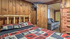 Interior de una cabaña de madera con una cama que tiene colcha a cuadros rojo y negro, cabecera de madera y c ómoda con cajones.