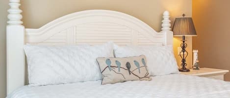 Un lit bien fait, avec une tête de lit blanche et un coussin décoratif orné de motifs d’oiseaux.
