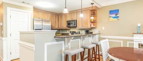 A kitchen with wooden cabinets, a stainless steel refrigerator, a microwave, and a large island with stools.
