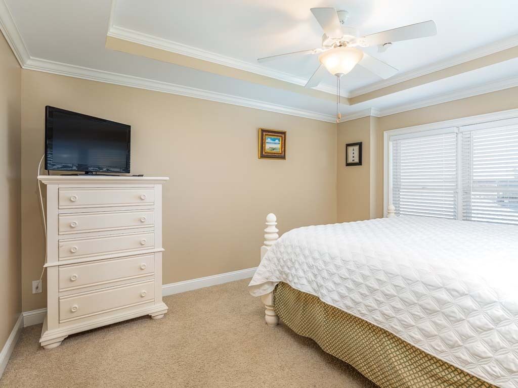 A bedroom with a bed, a dresser, a ceiling fan, and a television.