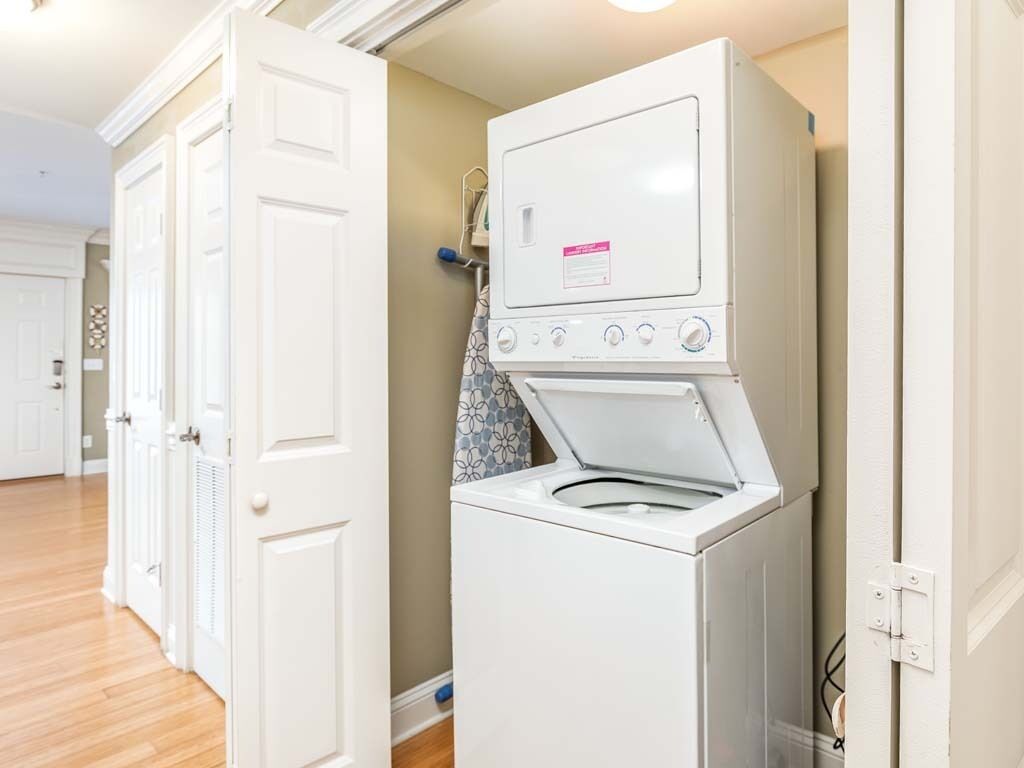 A laundry room with a front-loading washer and dryer, wooden flooring, and white doors.