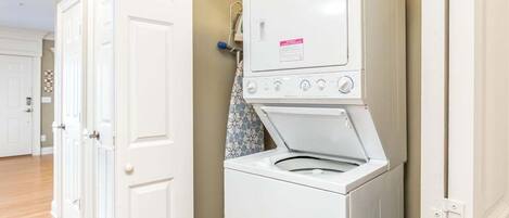 A laundry room with a front-loading washer and dryer, wooden flooring, and white doors.