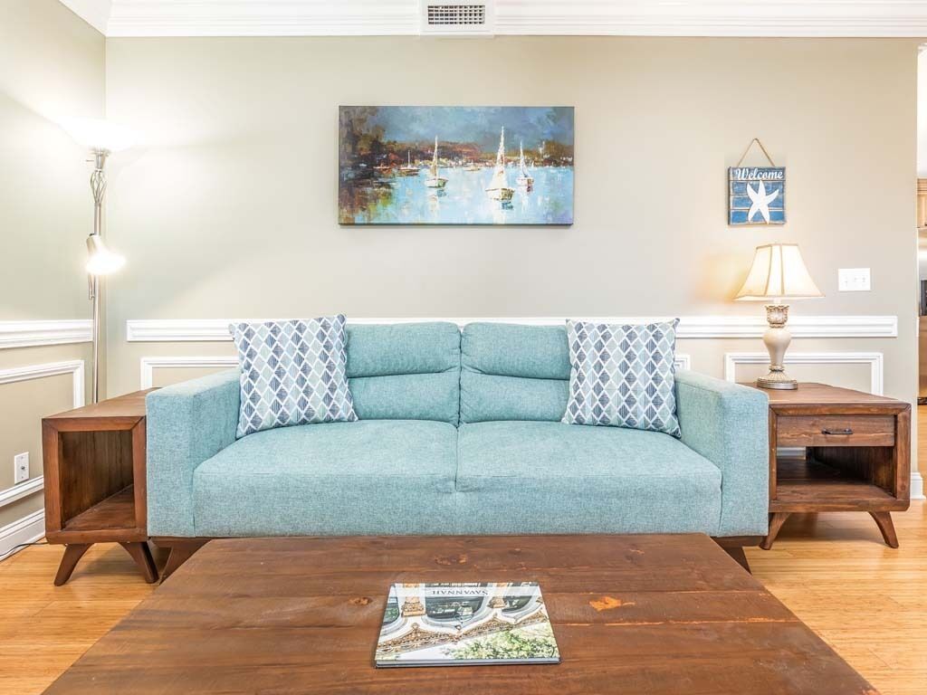 A living room with a teal sofa, wooden coffee table, and a painting of a harbor scene.