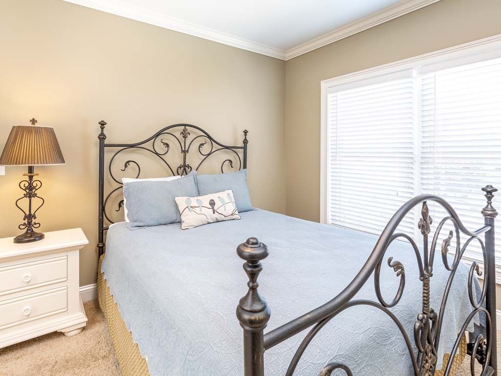 A bedroom with a bed, a nightstand, a lamp, and a window with blinds.