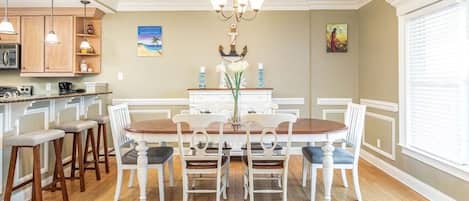 Un comedor con una mesa y sillas de madera, un candelabro y una cocina al fondo.