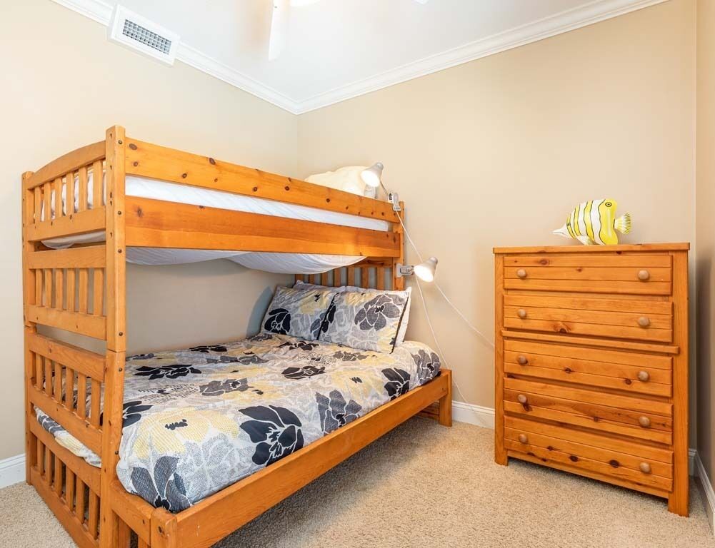 Una cama litera con colcha estampada, un aparador de madera con cajones y un pequeño pez de juguete encima.
