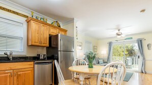 A kitchen with wooden cabinets, a stainless steel refrigerator, and a dining table with white chairs. - Silver Shores 4 by Tybee Vacation Rentals (Tybee Island)