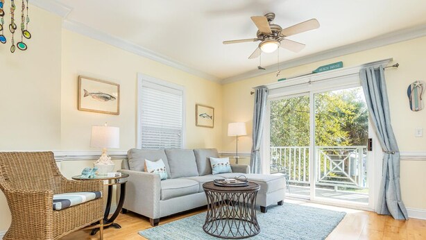 A living room with a wicker chair, a grey sofa, a round coffee table, and a ceiling fan. - Silver Shores 4 by Tybee Vacation Rentals (Tybee Island)