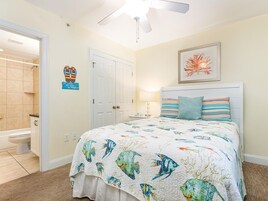 Une chambre à coucher comprenant un lit, un ventilateur de plafond, une porte, une salle de bain avec des toilettes et un élément décoratif mural.