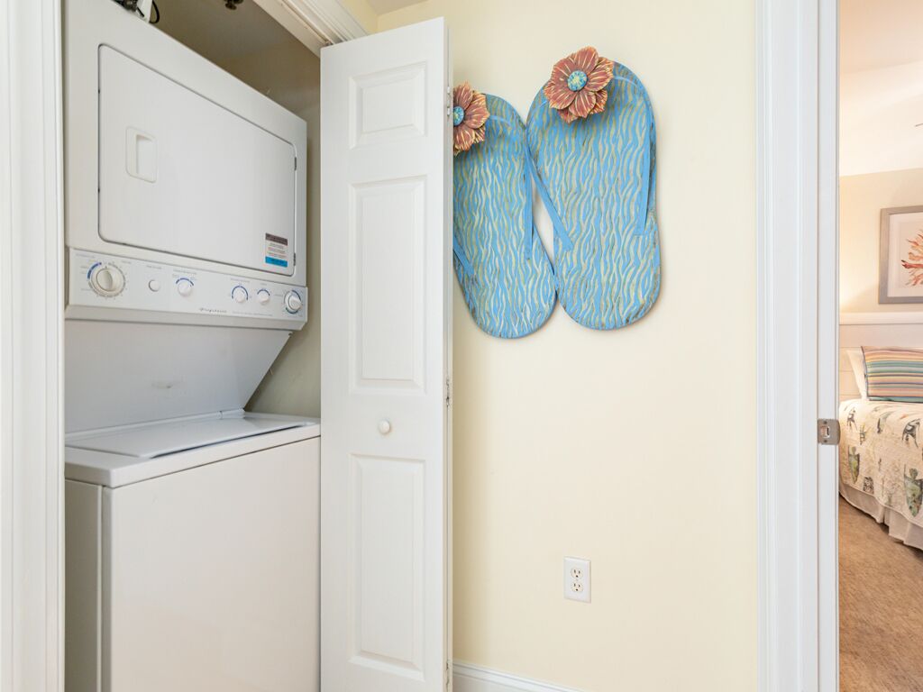 A laundry room with a white washer and dryer, a door, and a wall-mounted pair of blue and white patterned flip-flops.