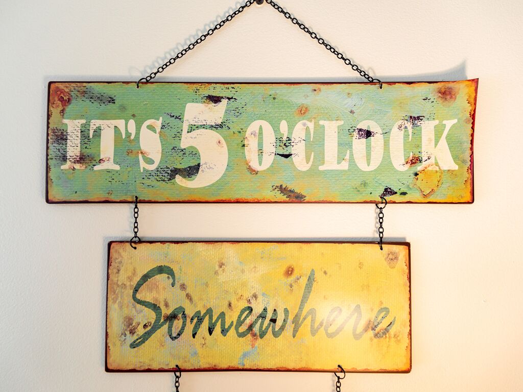 A rustic sign with the text "IT'S 5 O'CLOCK Somewhere" mounted on a wall.