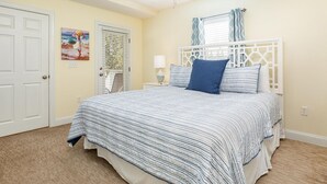 A bedroom with a bed, a ceiling fan, a window with curtains, and a door. - Silver Shores 4 by Tybee Vacation Rentals (Tybee Island)