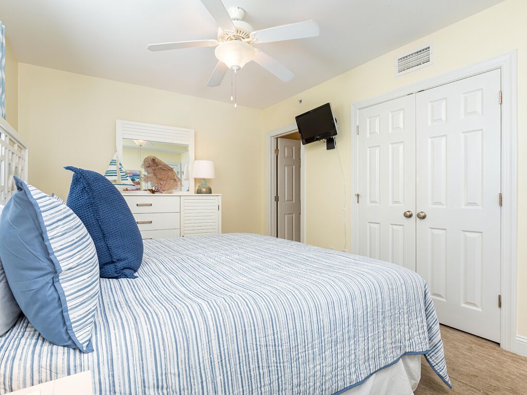 A bedroom with a bed, a ceiling fan, a television mounted on the wall, and a door.