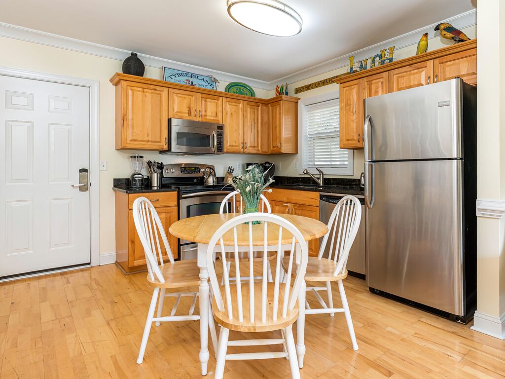 Una cocina con gabinetes de madera, un refrigerador de acero inoxidable, un microondas y una mesa de comedor con sillas blancas.