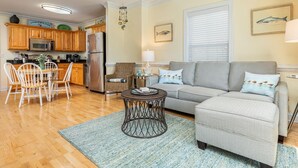 A living room with a grey sofa, a coffee table, and a dining area with wooden chairs. - Silver Shores 4 by Tybee Vacation Rentals (Tybee Island)