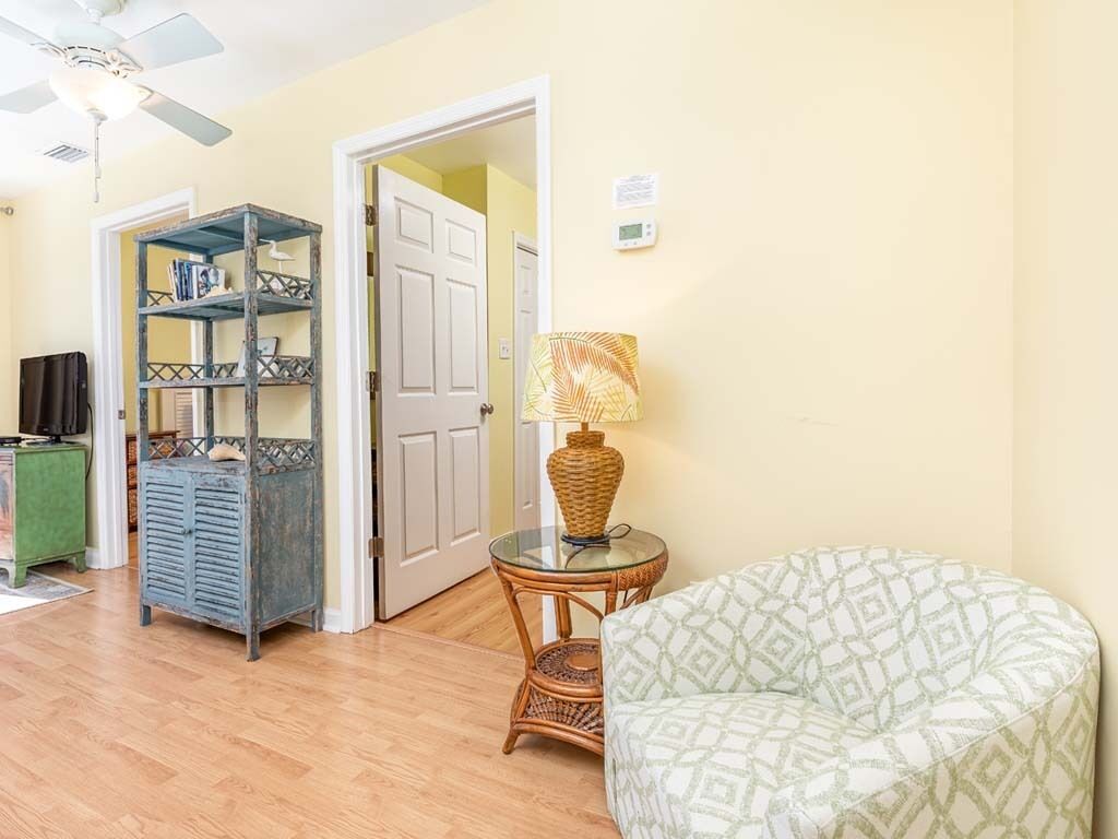 A room with a patterned armchair, a wicker side table with a lamp, a bookshelf, and a green cabinet.