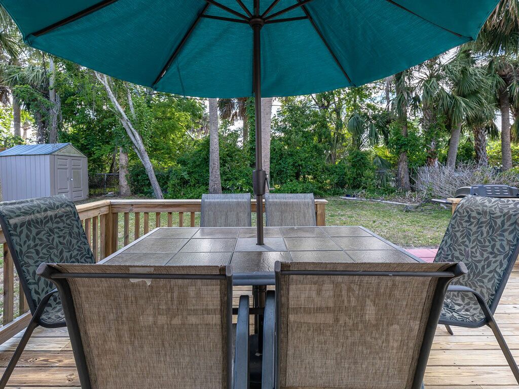 Eine Holzterrasse mit Tisch und Stühlen, umgeben von üppiger Vegetation und einem kleinen Schuppen.
