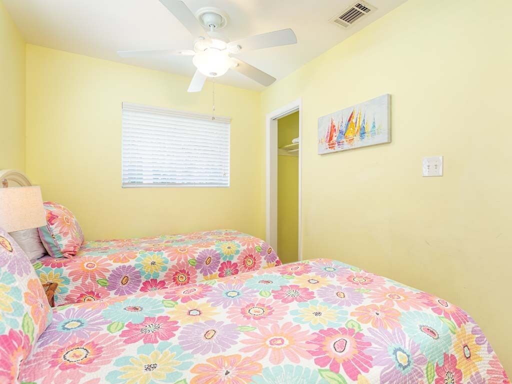 Une chambre avec deux lits, un ventilateur de plafond, une fenêtre avec des stores et un tableau au mur.