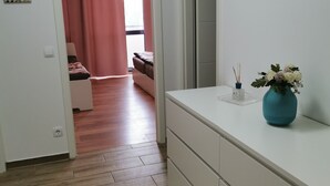 Een kamer met een houten vloer, een witte dressoir, een roze gordijn en een kleine vaas met bloemen op het dressoir.