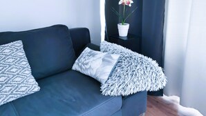 Een moderne woonkamer met een donkerblauwe bank, twee gestreepte kussens, een zachte witte plaid en een potorkidee op een klein zwart bijzettafeltje.