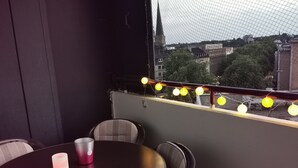 Een balkon met een tafel, stoelen, een kaars en sfeerverlichting.