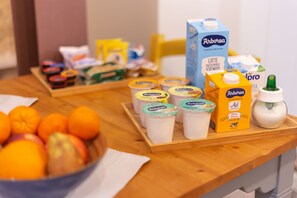 Una mesa de desayuno con diversos alimentos y bebidas, incluyendo un bol de fruta, cartones de leche y recipientes de jugo.