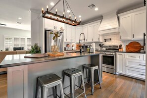 Una cocina moderna con gabinetes blancos, electrodomésticos de acero inoxidable y una isla central con taburetes.