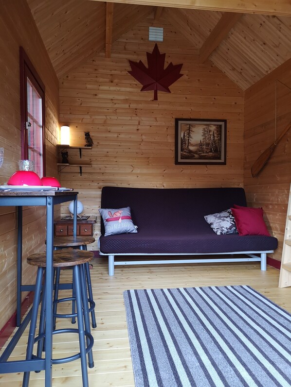 A cozy cabin interior with a wooden interior, a couch with pillows, a table with chairs, and a framed picture on the wall.