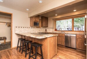 A modern kitchen with a large island, bar stools, wooden cabinets, a microwave, and a dishwasher.