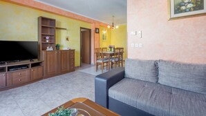 A living room with a sofa, TV, wooden cabinets, and a dining area with chairs and a table. - Holiday apartment with sea view (Poreč)