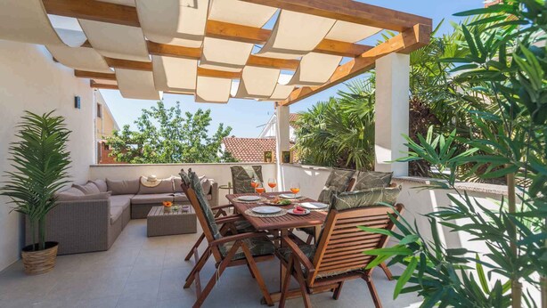 An outdoor patio with a wooden table and chairs, a sofa, and potted plants. - Holiday apartment with sea view (Poreč)