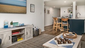 Una sala de estar moderna con un televisor grande, un comedor con sillas de madera y una cocina con encimera azul.