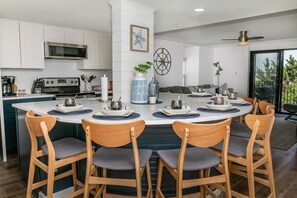 A modern kitchen with white cabinets, a central island with bar stools, a microwave, and a stove.