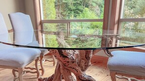A dining table with a glass top and a unique wooden base, surrounded by upholstered chairs.