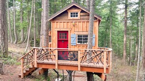 A wooden treehouse with a red door and blue shutters, accessible by a wooden staircase.