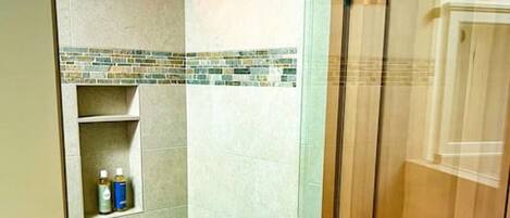 A shower area with a glass door, a shelf with toiletries, and a mosaic tile backsplash.