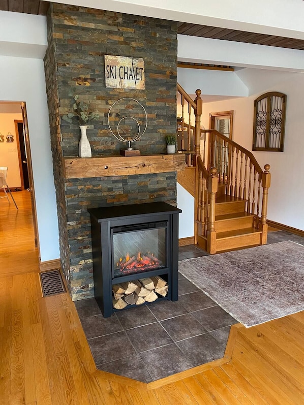 A stone fireplace with a sign reading "SKI CHAMET," a wooden staircase, and a rug on the floor.