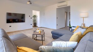 A modern living room with a grey sofa, a coffee table, and a TV mounted on the wall. There is a potted plant and a lamp in the room. - Stunning  villa for 8 people with A/C, WIFI, private pool, TV and terrace (Šegotici)
