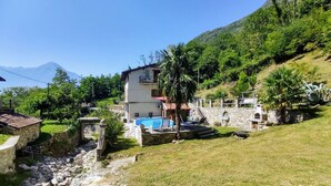 Una casa de dos pisos con piscina, paredes de piedra y montañas al fondo.
