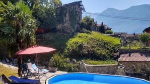 Una piscina con sillas de descanso y una sombrilla, rodeada de vegetación y edificios de piedra.