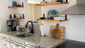 A modern kitchen with granite countertops, stainless steel appliances, and wooden shelves.