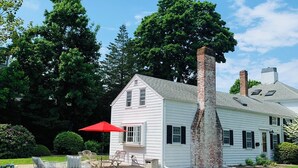 A white house with a brick chimney, surrounded by a well-maintained lawn and trees.