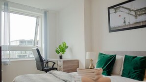 Ein Hotelzimmer mit Bett, Schreibtisch, Stuhl, Fenster und Pflanze.