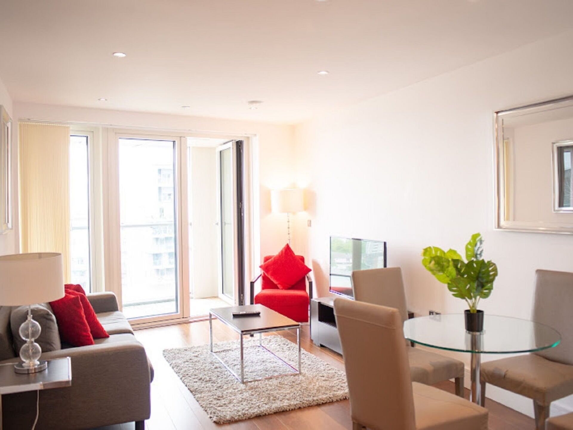 Una sala de estar moderna con sofá, sillón, mesa de centro de vidrio y una mesita con lámpara.