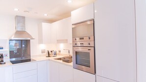 Eine moderne Küche mit weißen Schränken, einer Edelstahl-Dunstabzugshaube und einem Backofen mit zwei Garstufen.