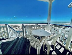 A balcony with a table and chairs, overlooking a beach.