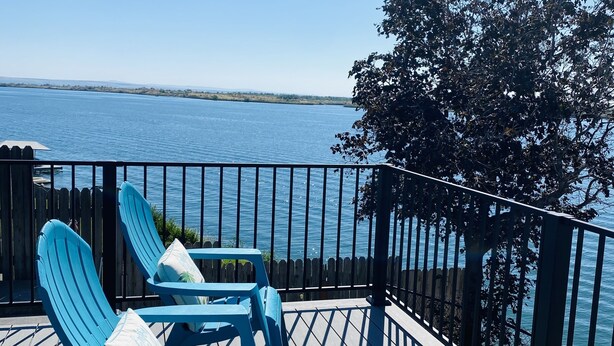 A wooden deck with two blue Adirondack chairs and a view of a calm body of water. - Spacious 4 bedroom lakefront house: with private dock and pool. (Moses Lake)